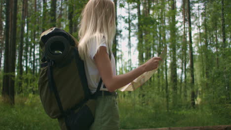 A-young-woman-with-a-map-is-walking-through-the-forest-traveling-with-a-backpack-in-slow-motion.-Traveler-in-shorts-in-the-woods